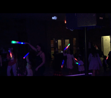 People dancing with glowing light sticks in a dark outdoor setting.