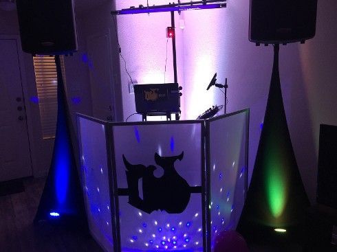 DJ setup with speakers, lights, and a console, illuminated with blue and green colors.