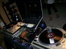 DJ setup with turntables, laptop, and person in background.