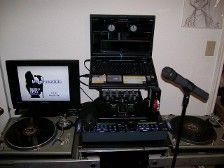 DJ setup with turntables, mixer, laptop, monitor, and microphone in a room.