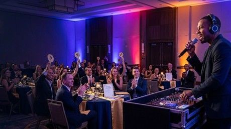 DJ performing for a seated audience at a dimly lit event with purple and blue lighting