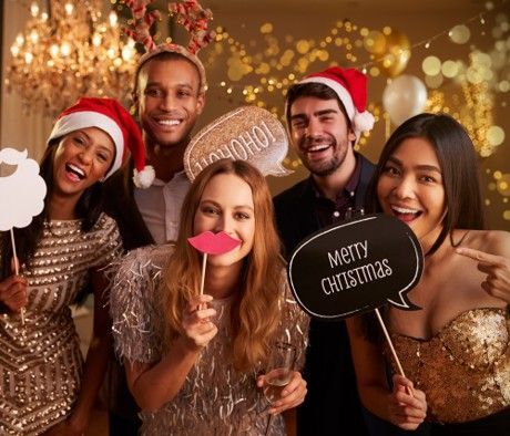 Five friends in festive hats and party attire posing with holiday signs at a Christmas celebration