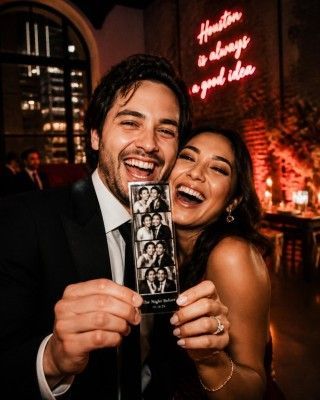 Smiling couple at a party, holding a photo booth strip in warm, dim lighting