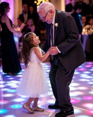 Elderly man dancing with a young girl in a white dress on a colorful lit dance floor