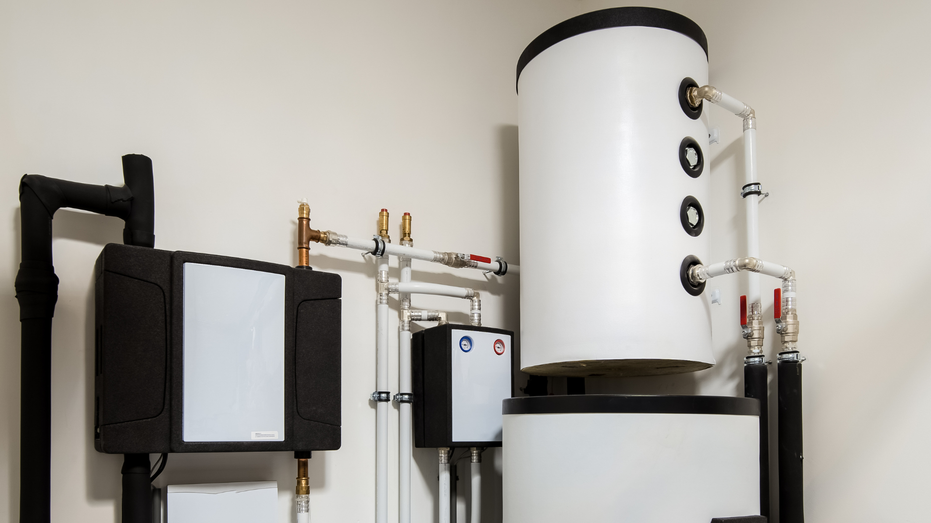 Wall-mounted white tanks and black equipment connected by pipes in a utility room