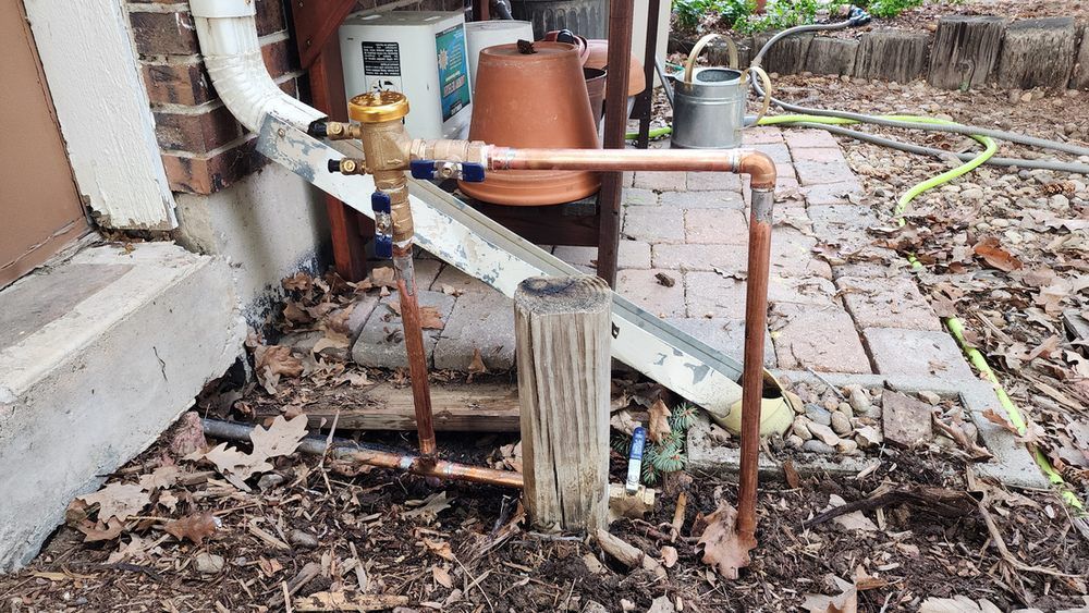 A copper pipe is sitting on the ground next to a brick wall.