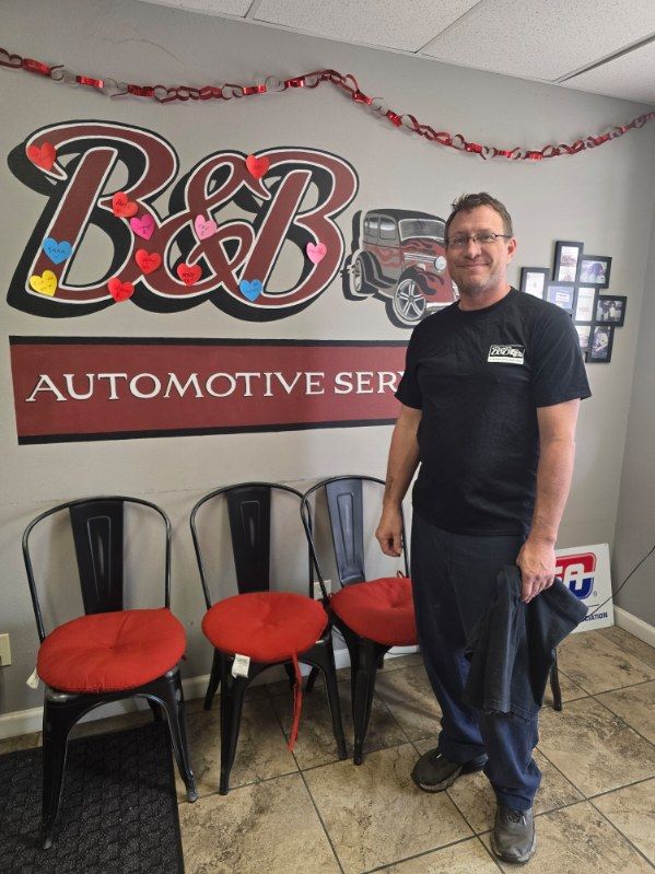 Man standing in an automotive service shop beside a B&B sign and red chairs