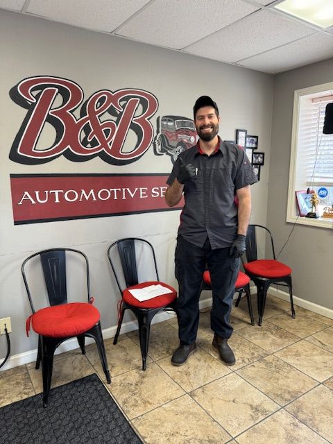 Man standing in a B&B Automotive Services lobby beside red chairs and a wall logo