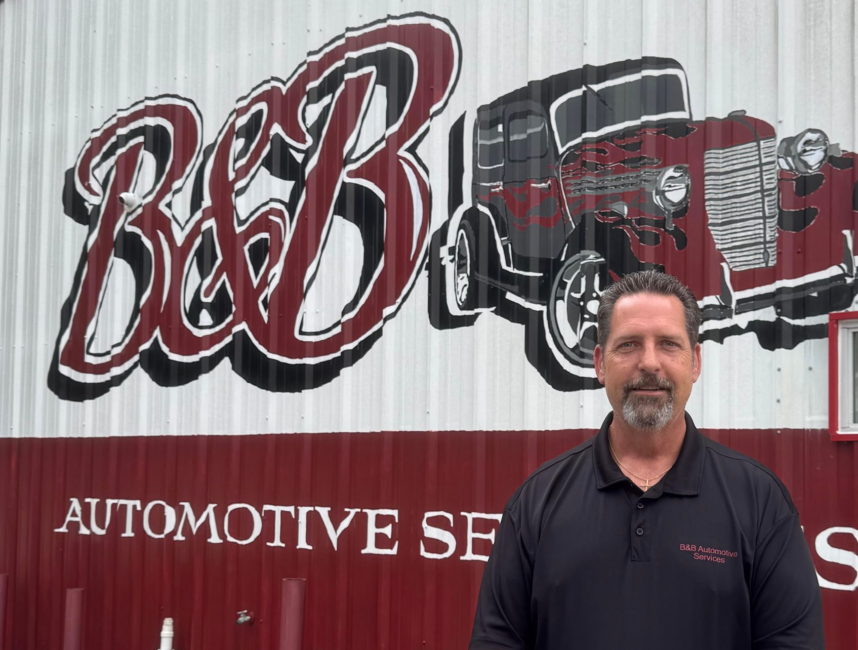 Man standing before B&B Automotive Service mural with red vintage truck and sign