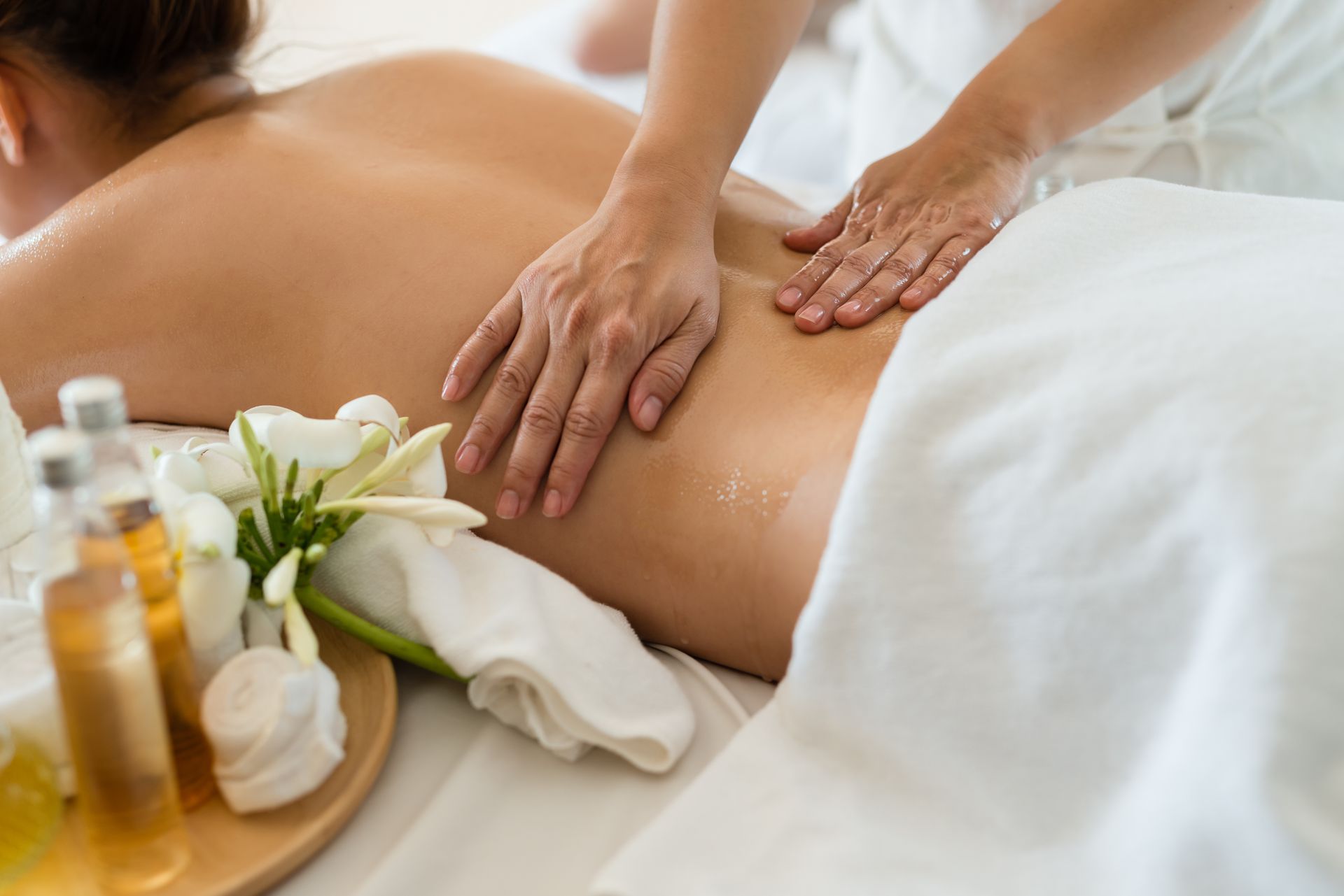 Massage therapist giving a back massage with oils and white flowers in a spa setting Massage therapist giving a back massage with oils and white flowers in a spa setting
