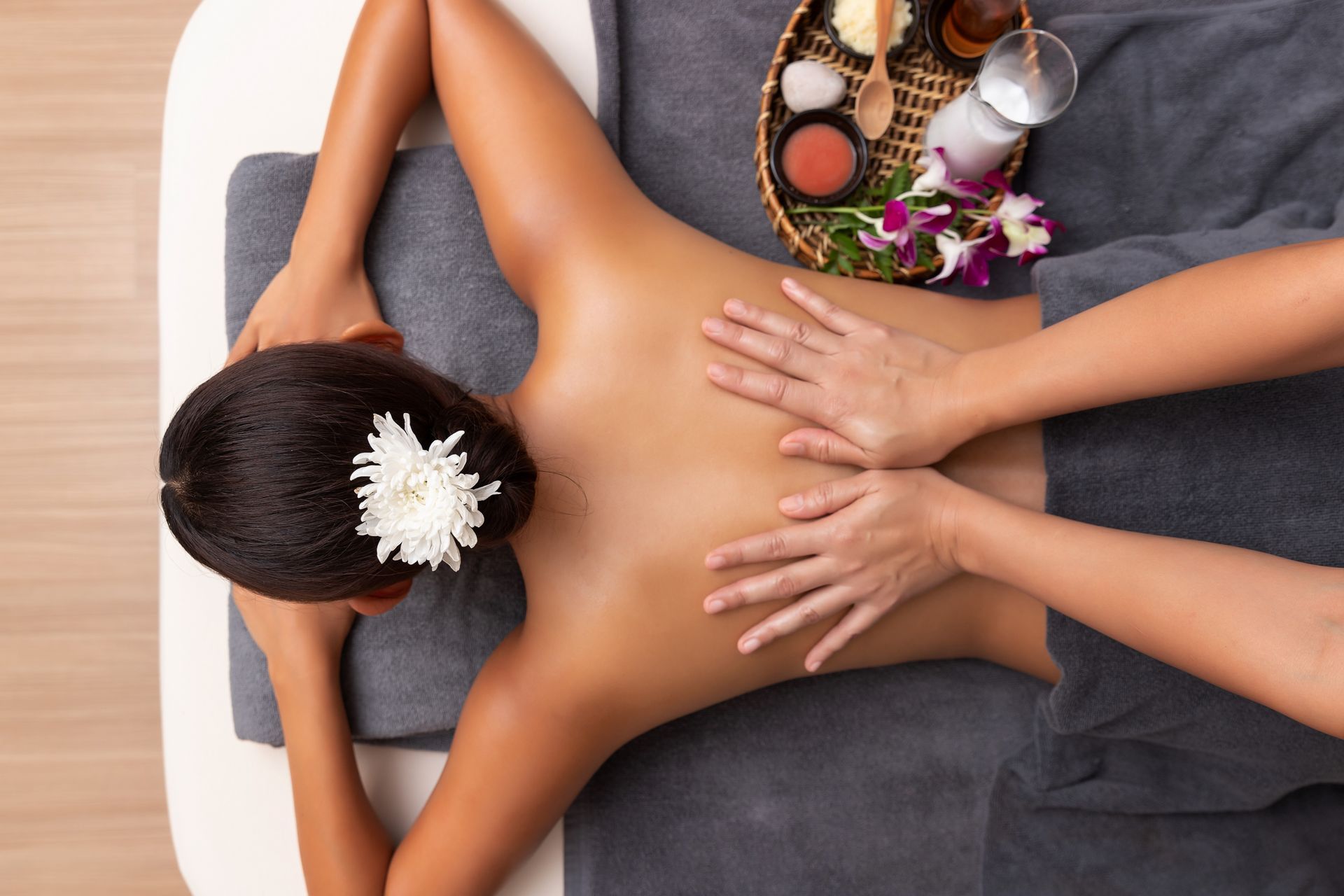 Back massage with spa stones, flowers, and towels on a woman lying face down on a massage table Back massage with spa stones, flowers, and towels on a woman lying face down on a massage table