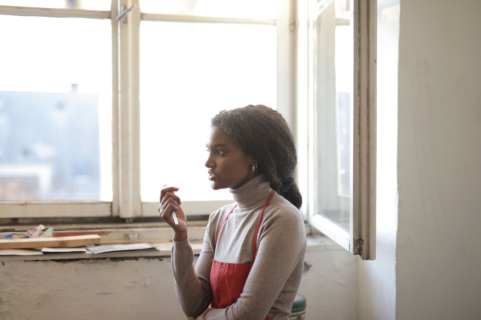 Femme pensive devant une fenêtre lumineuse, une tasse à la main, réfléchissant à ses doutes amoureux