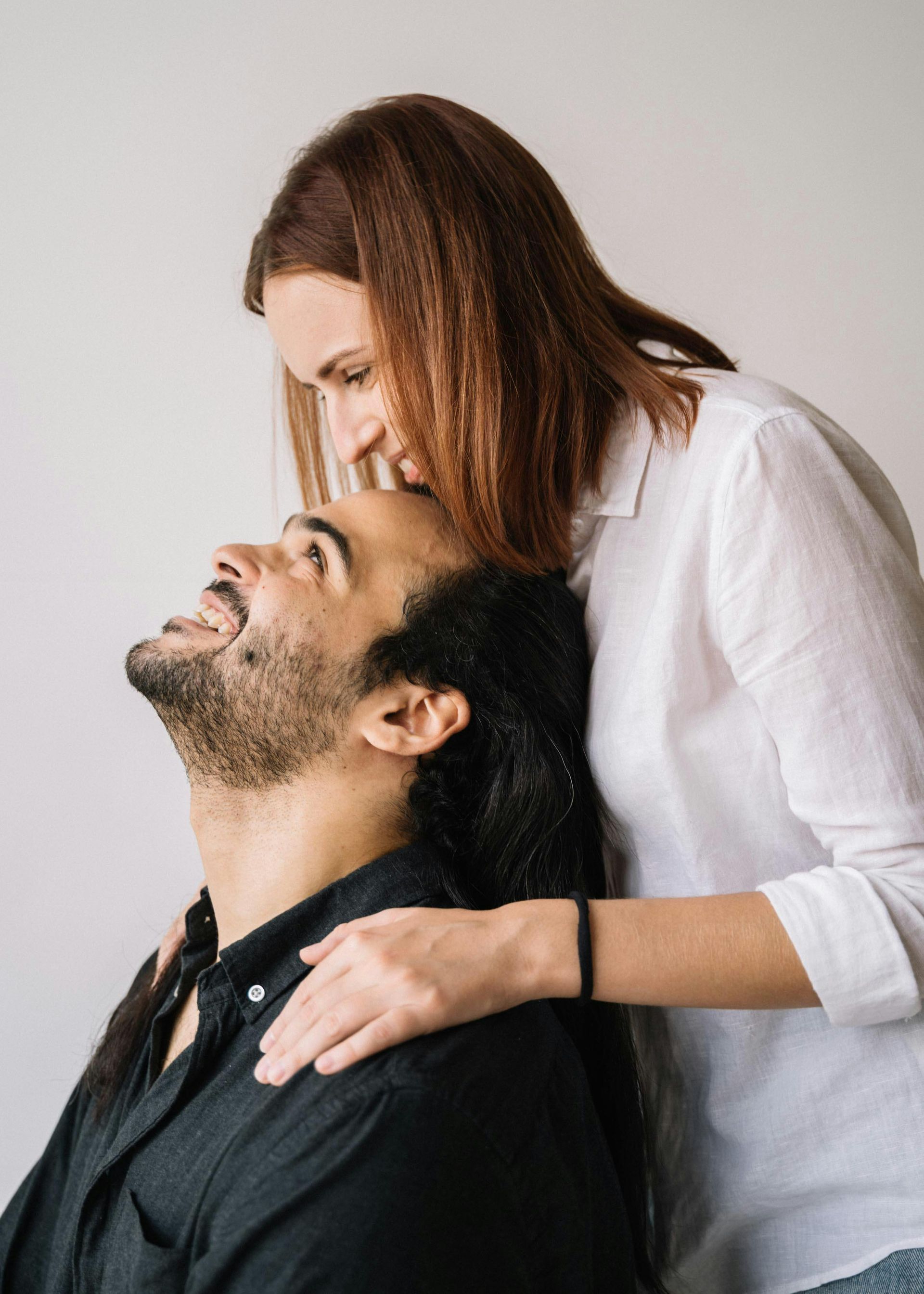 Une femme examine doucement le visage d'un homme assis dans un décor lumineux et minimaliste.