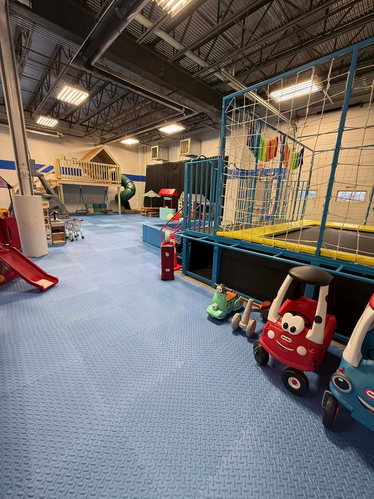 Indoor playground with climbing net, red slide, play cars, and blue padded flooring