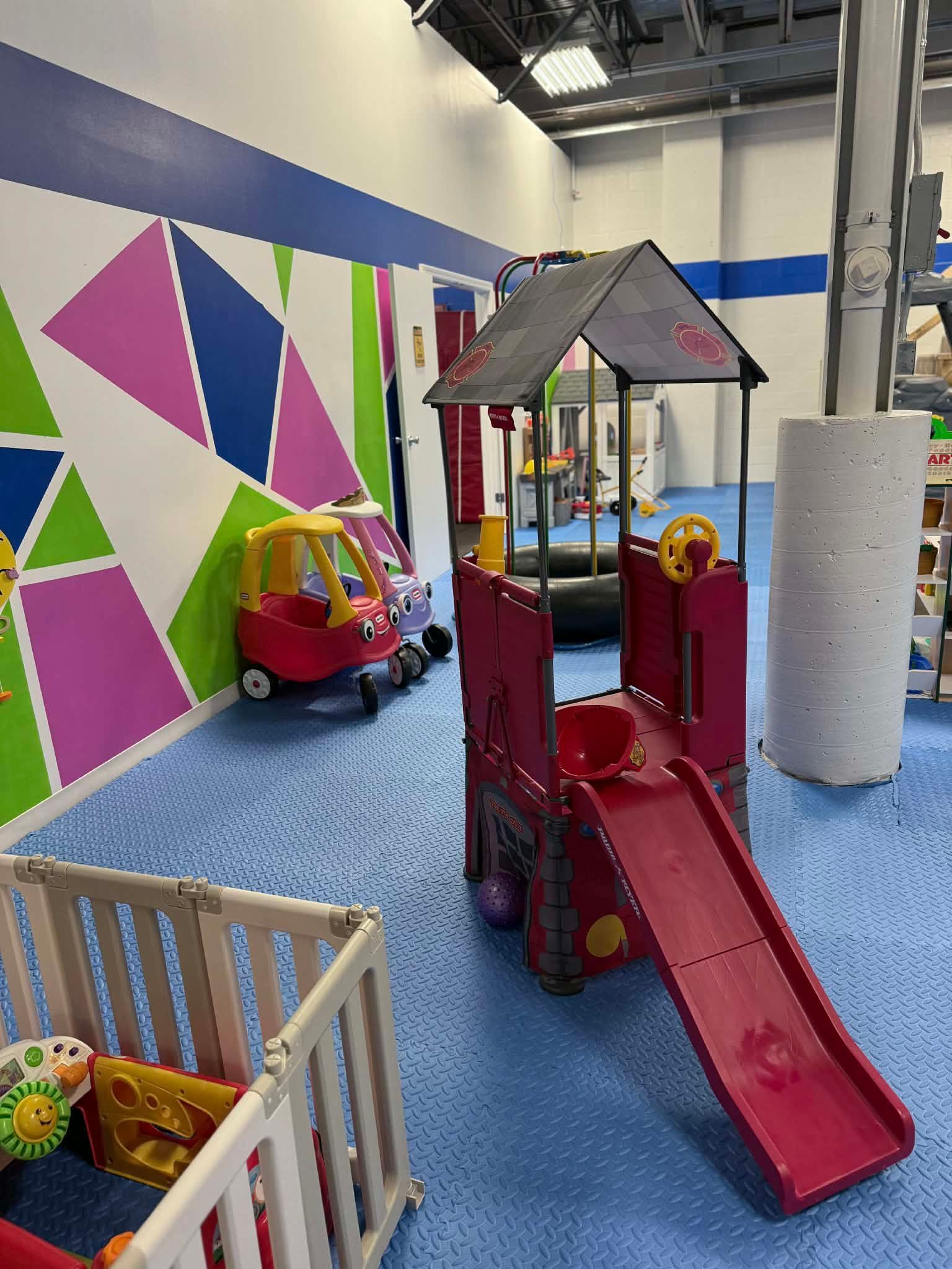 Indoor play area with red slide, toy house, ride-on cars, and colorful geometric wall art