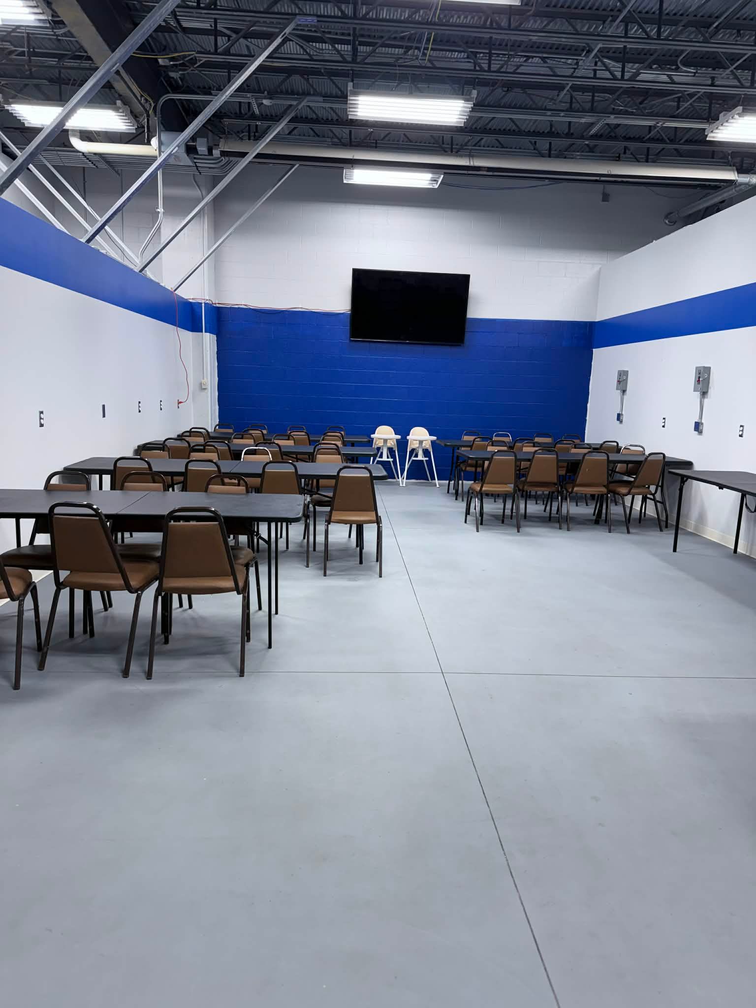 Empty gymnasium with folding chairs arranged facing a wall-mounted screen and blue stage backdrop