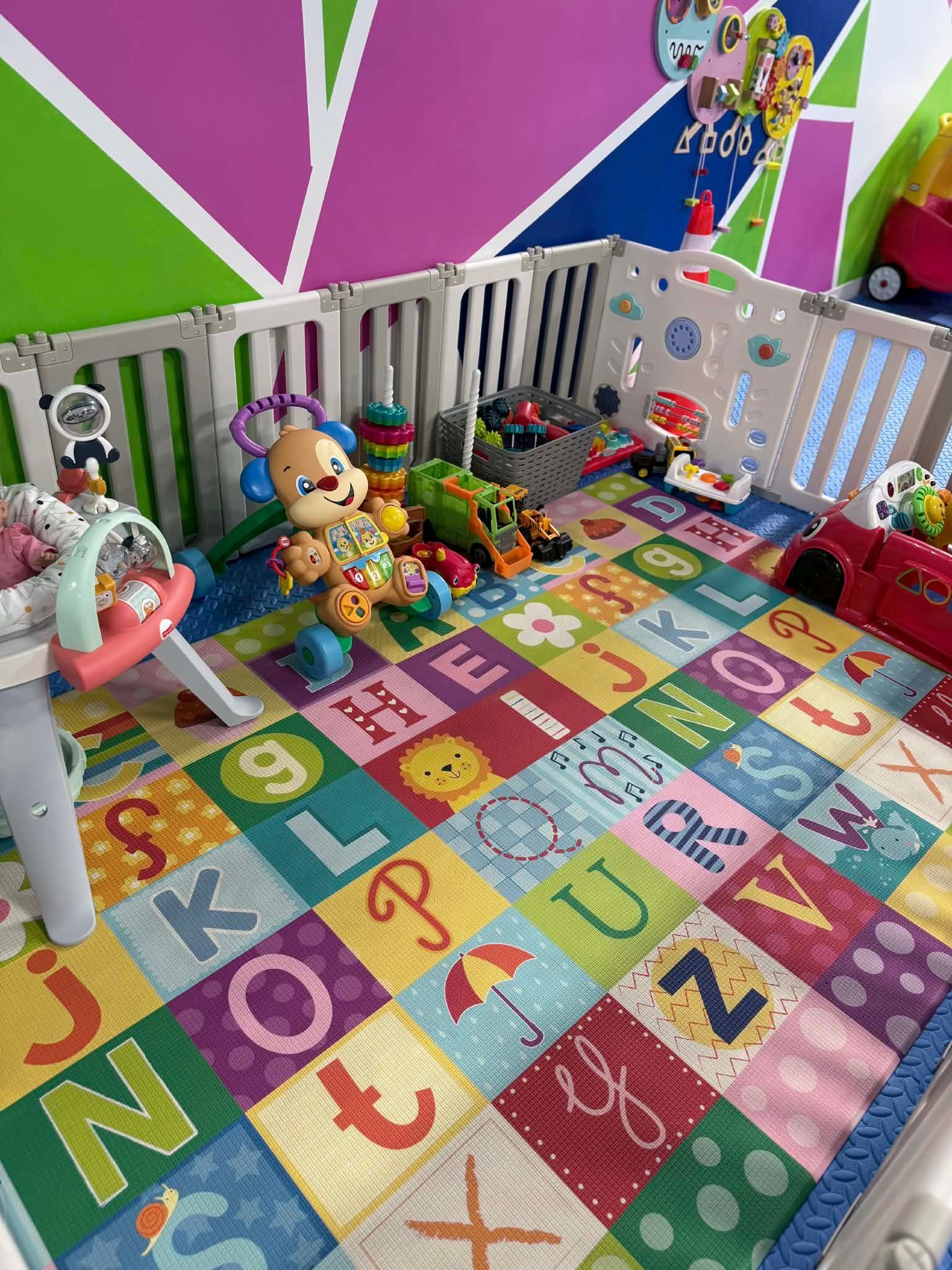 Colorful playpen with toys, alphabet rug, and white fence in a bright child’s room