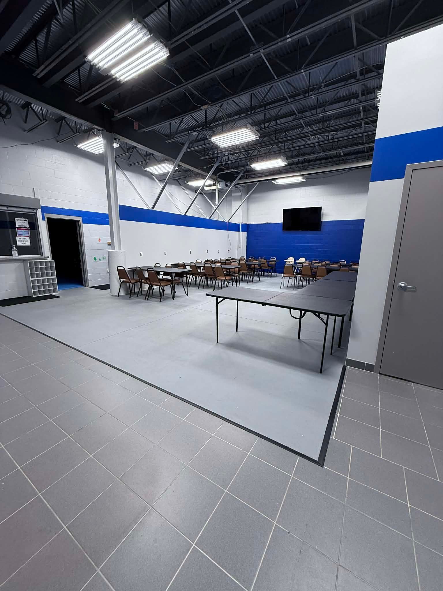 Large empty conference room with rows of tables, black chairs, and blue-and-white walls under exposed ceiling lights