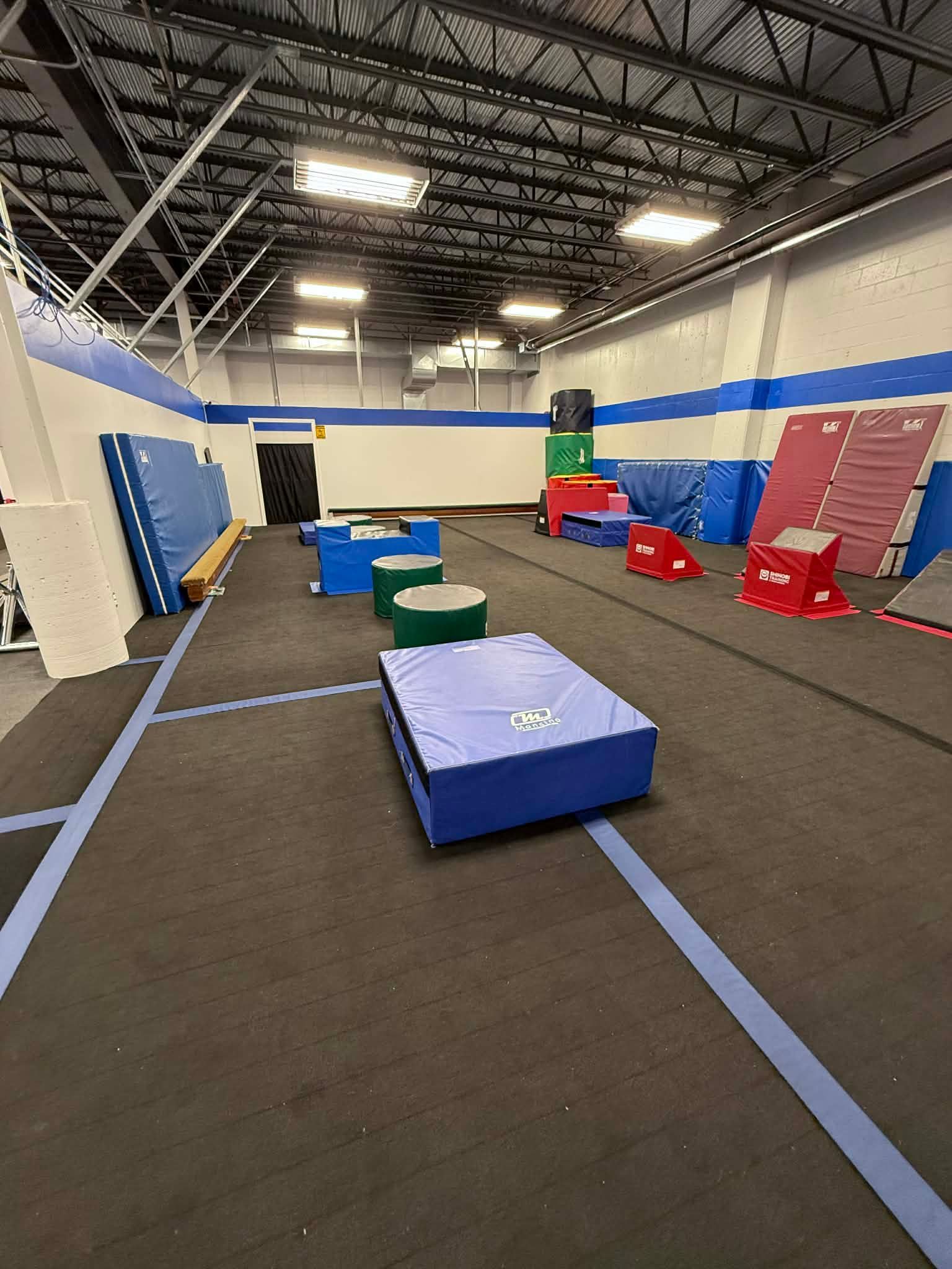 Indoor gym with foam obstacles, mats, and a padded floor under bright ceiling lights