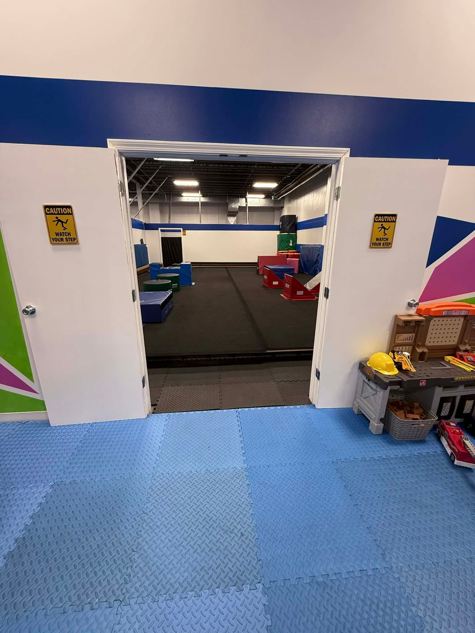 Blue-tiled gym entryway with an open doorway to an exercise area and colorful play equipment on both sides