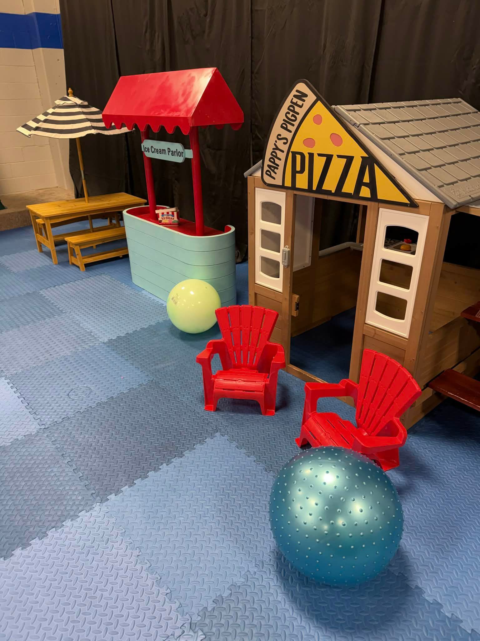 Indoor play area with toy huts, red chairs, and two colorful balls on blue carpet