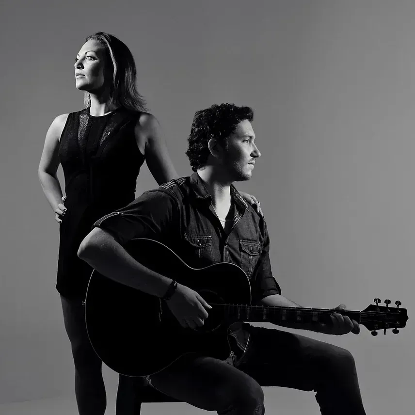 A man is playing a guitar while a woman stands behind him