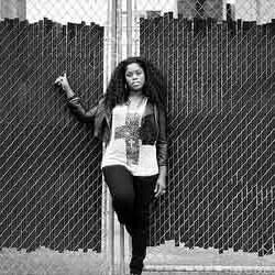 A woman is leaning against a chain link fence in a black and white photo.