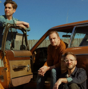 Three men are posing for a picture in front of a car