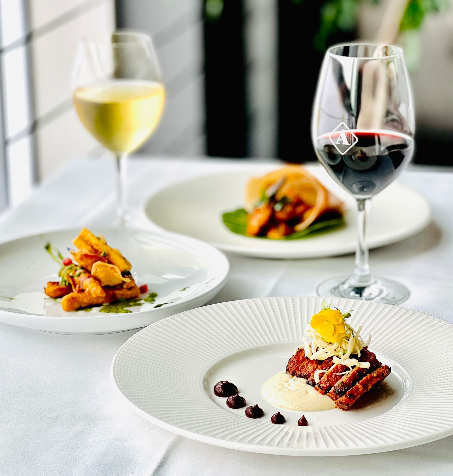 Three plates of food and two glasses of wine on a table
