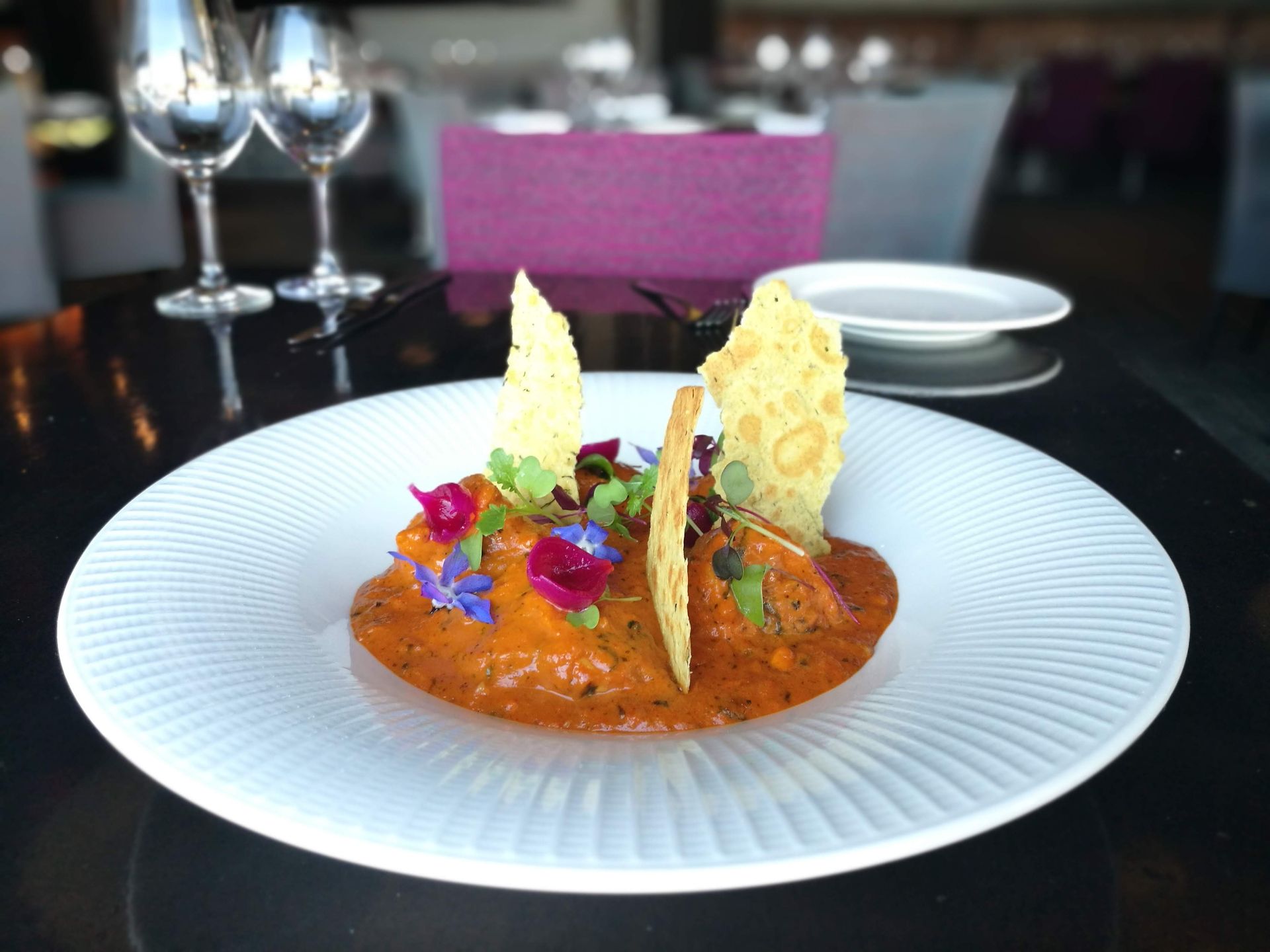 A plate of food on a table with wine glasses in the background
