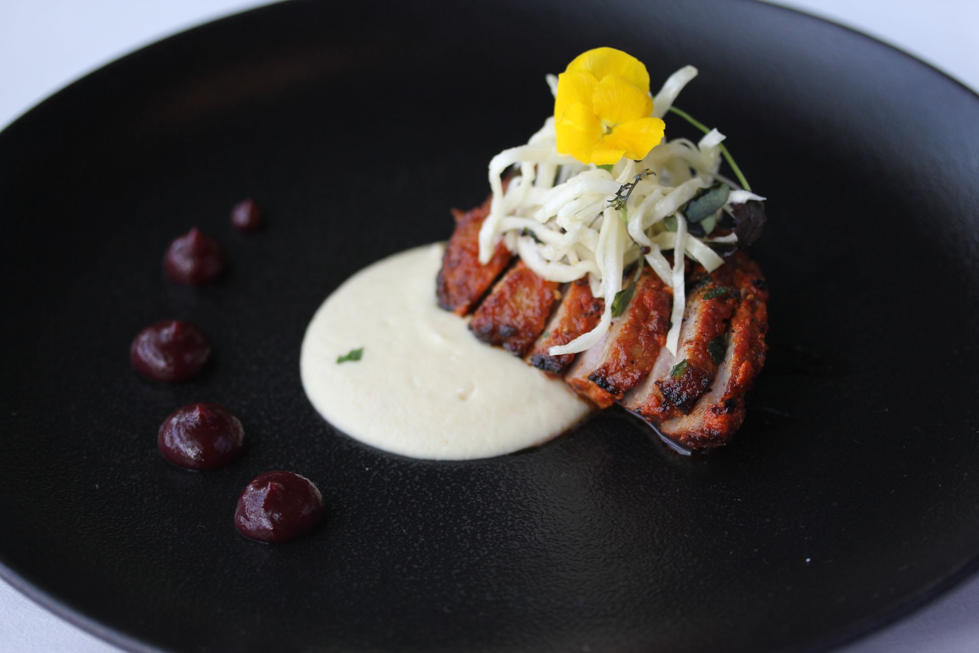 A black plate topped with a piece of meat and a flower