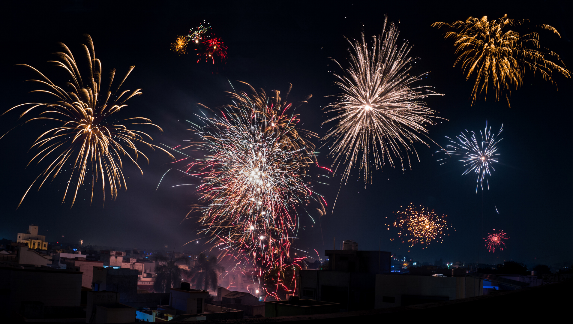 A bunch of fireworks are flying in the night sky over a city.