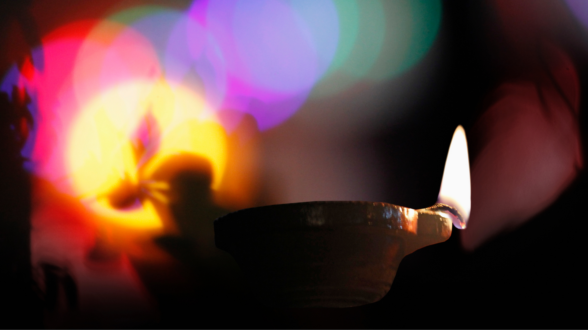 A candle is lit in a dark room with a colorful background