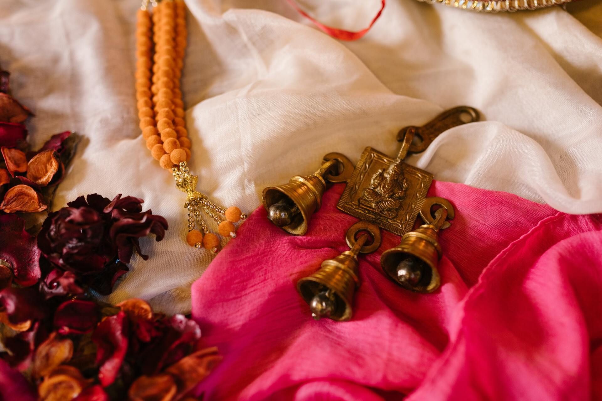 A close up of a necklace and bells on a pink cloth.