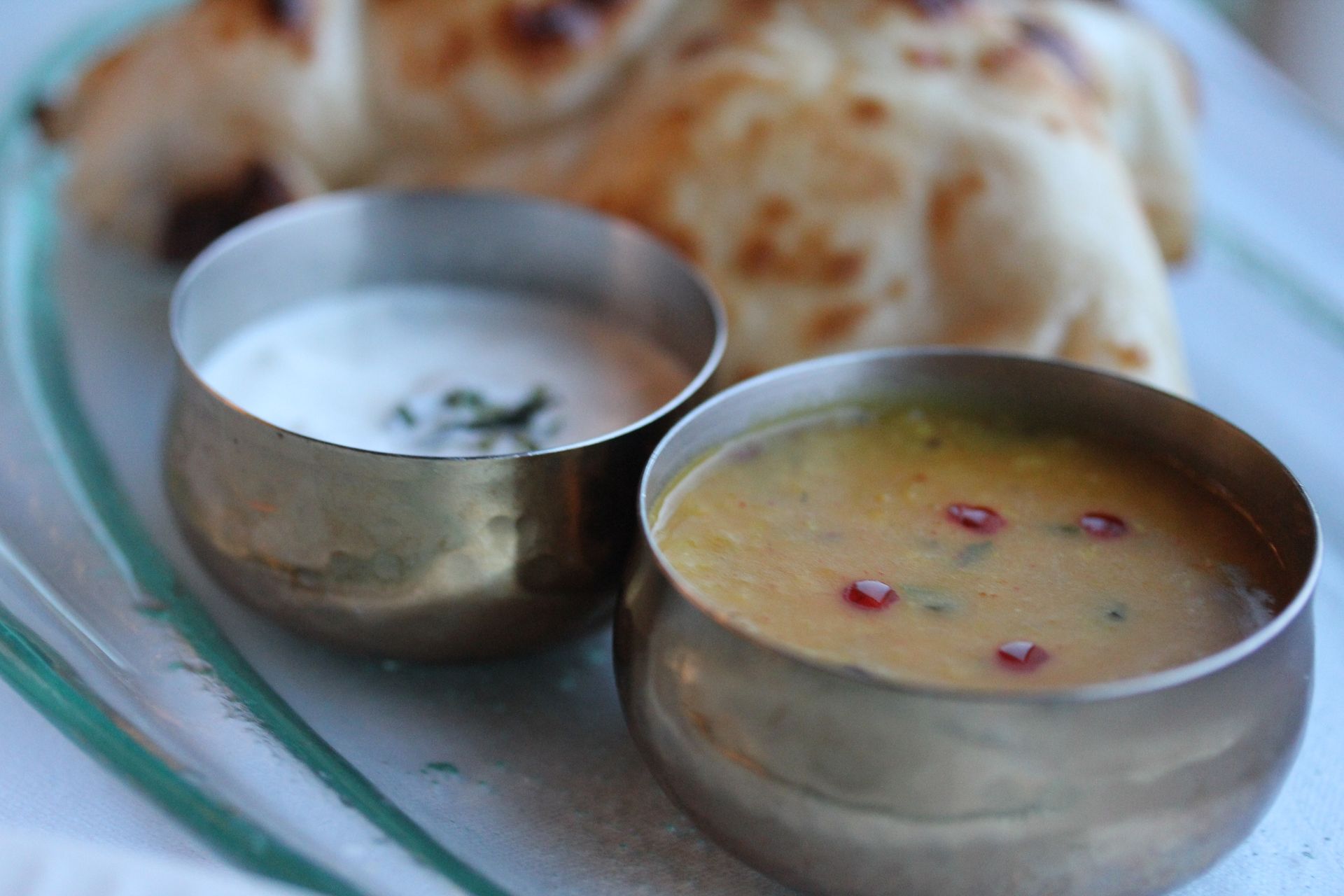 Two bowls of soup are on a plate with bread in the background