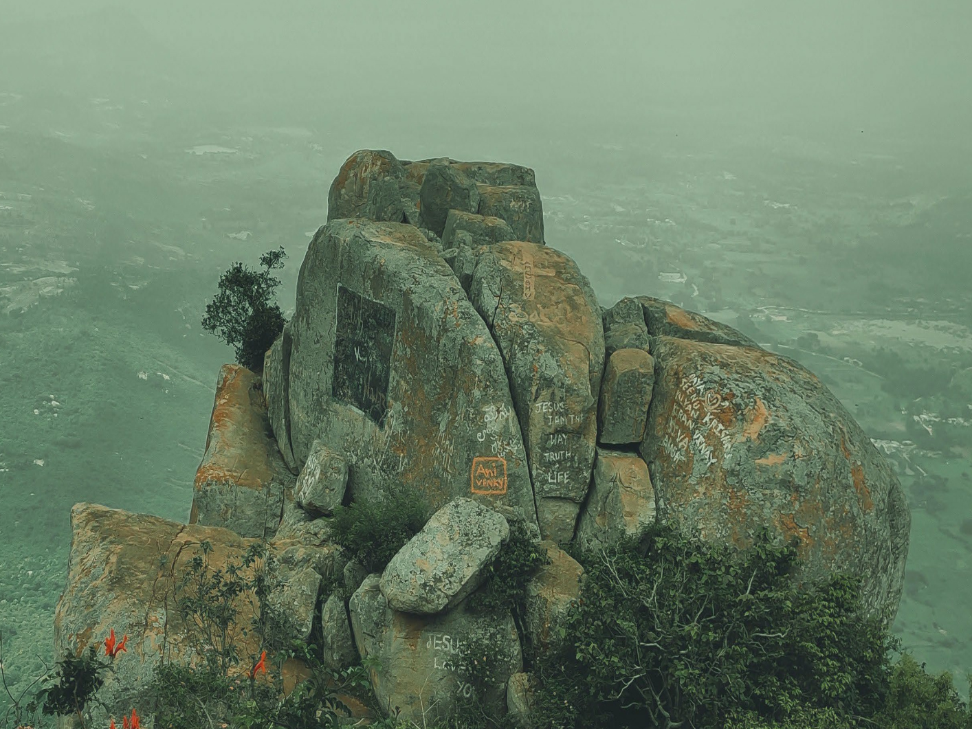 A large rock with graffiti on it is sitting on top of a mountain.