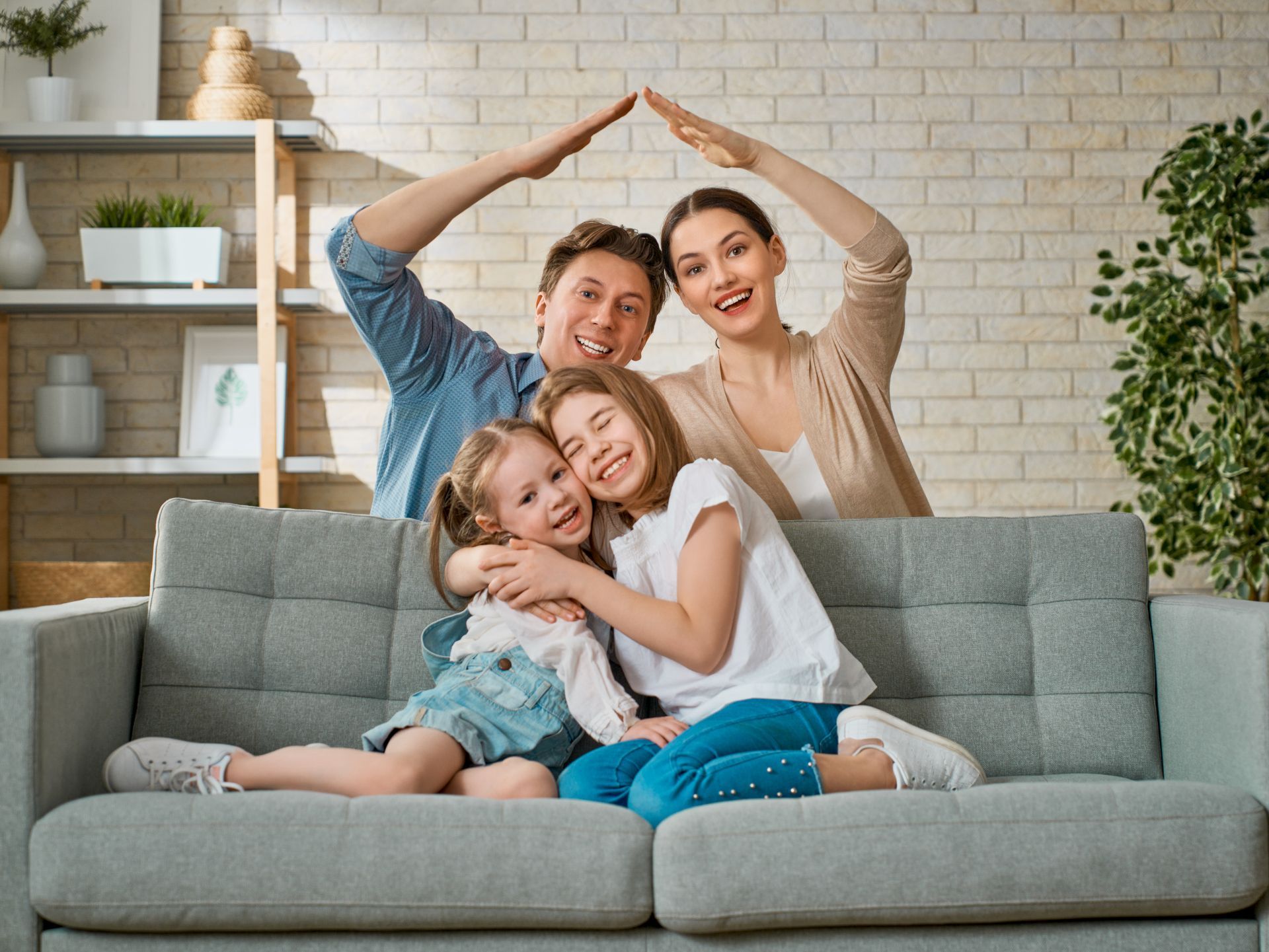 Smiling family of four on a gray couch, posing indoors with hands forming a heart shape above them