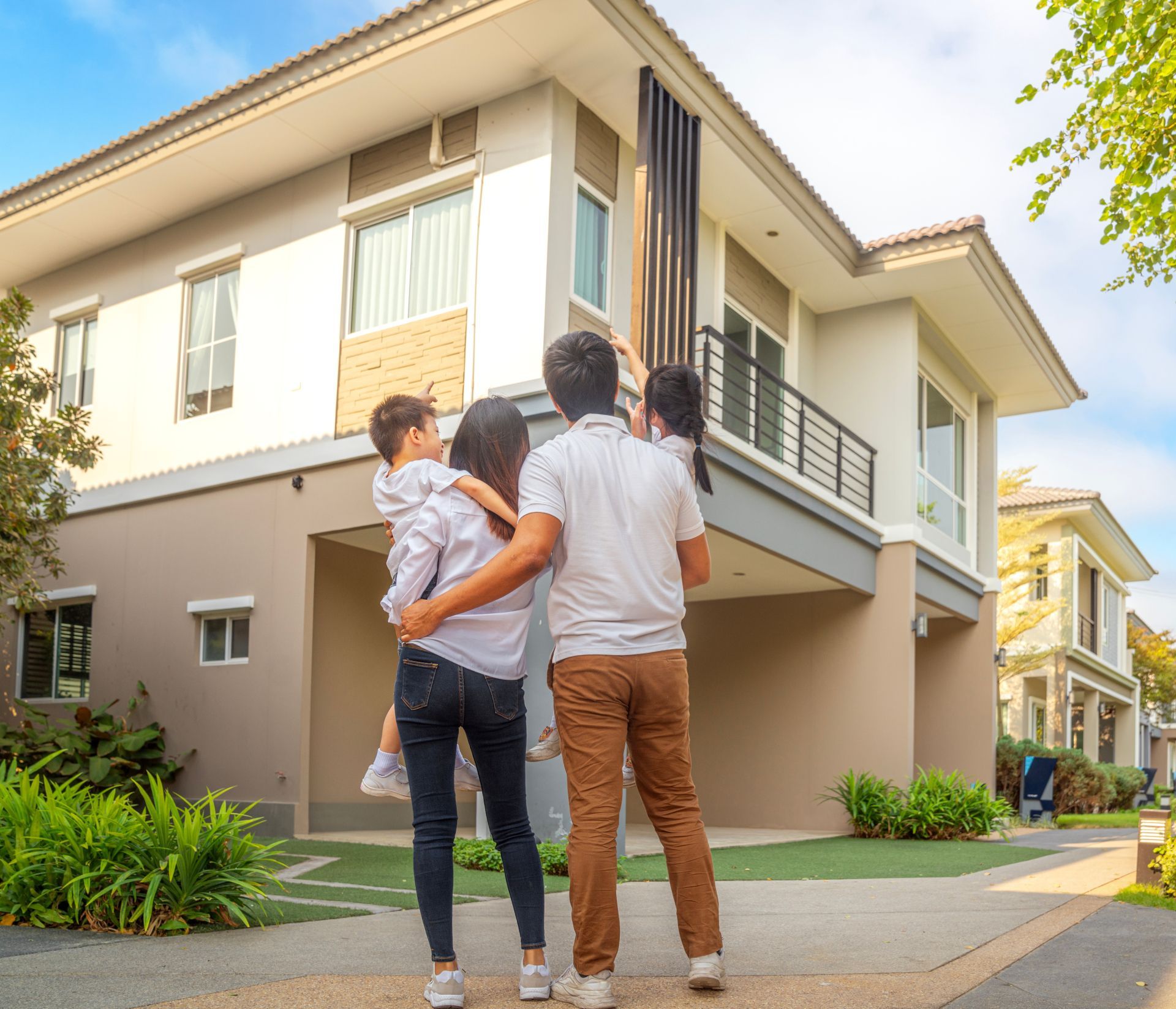 Two adults with a child stand outside a modern two-story house in a residential neighborhood.