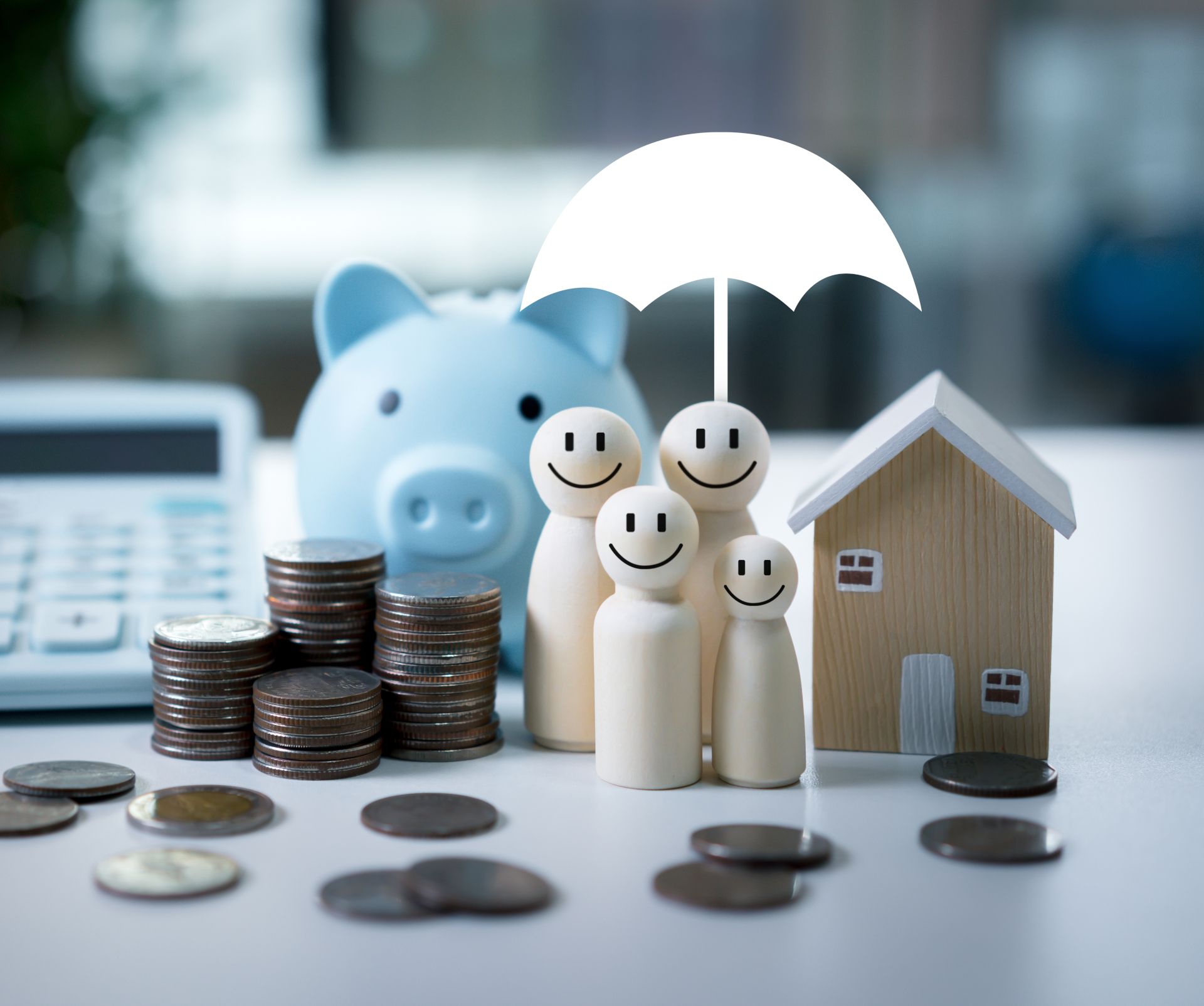 Piggy bank, family figures under umbrella, stacked coins, and a house model symbolizing insurance and savings