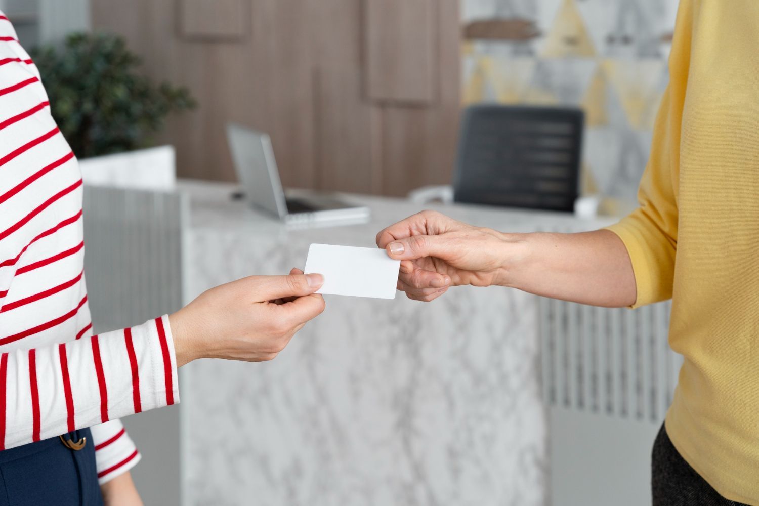 Person in striped shirt hands a blank card to another person in yellow shirt at a reception desk.