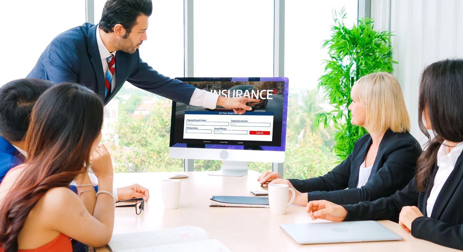 Business meeting with man pointing to insurance website on a computer screen.
