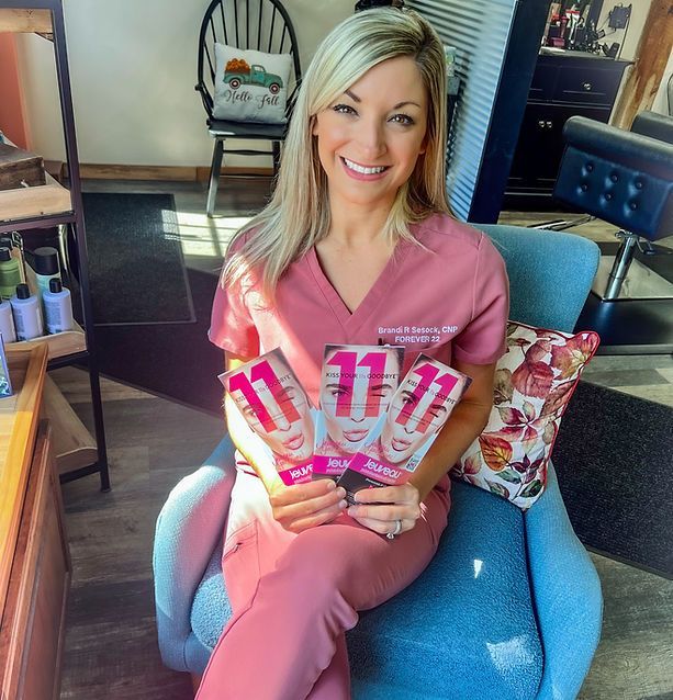Woman in pink scrubs, holding cards, smiling, seated in a blue chair, indoors.
