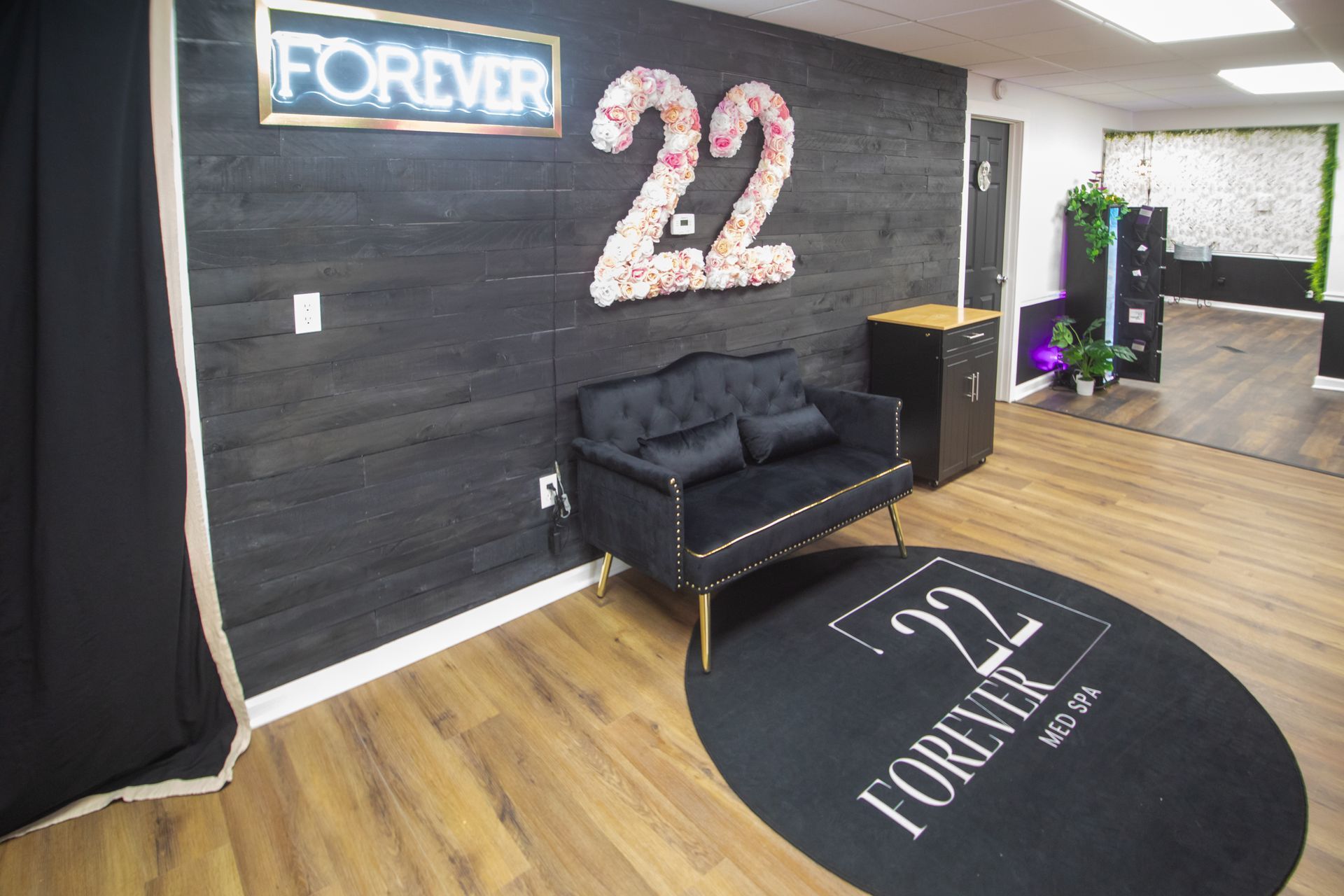 Woman examining her face in a mirror, held by a healthcare provider. Interior clinic setting with a black accent wall.