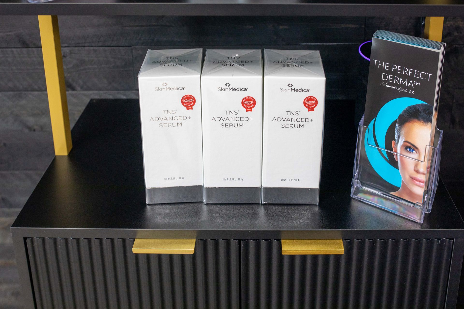 Three white product boxes with red seals on a shelf, next to a brochure with a woman's face.