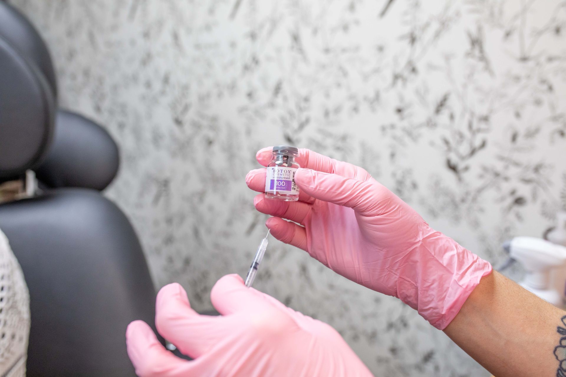 Gloved hands holding a vial and syringe, preparing an injection in a treatment room.