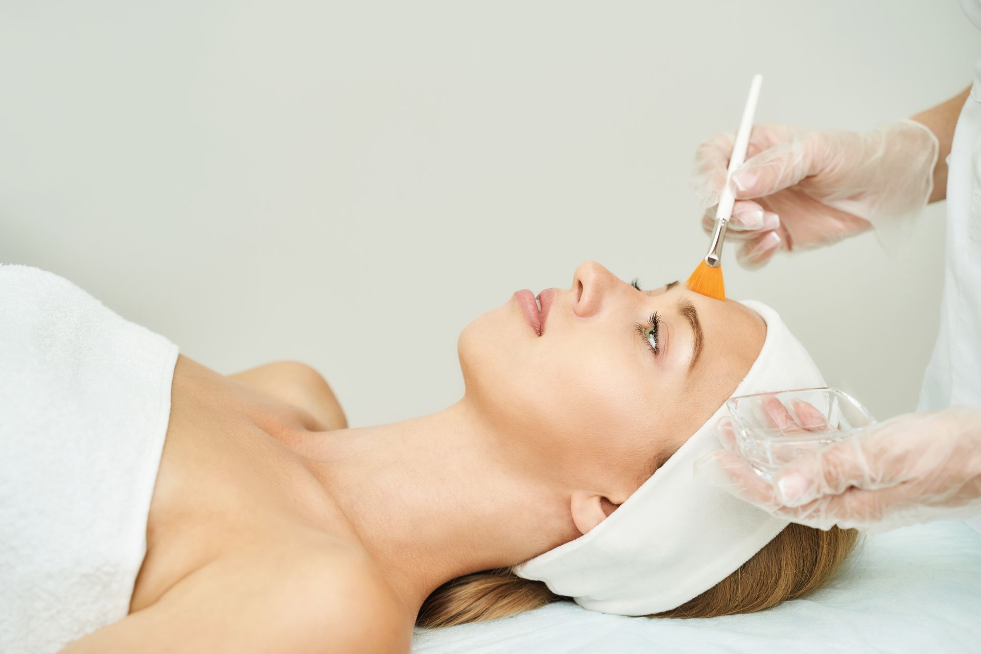 Woman receiving facial treatment, being administered with a brush in a spa setting.
