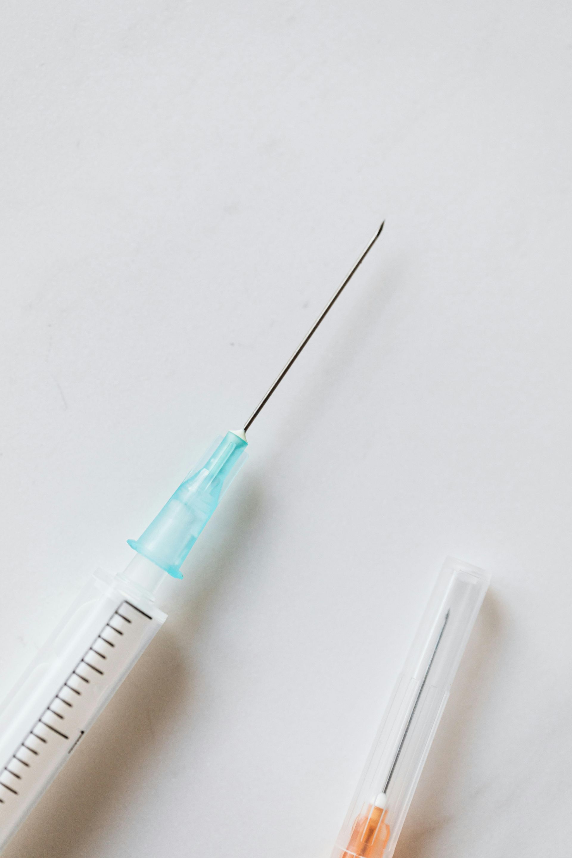 Syringe with a needle and orange needle cap on a white surface.