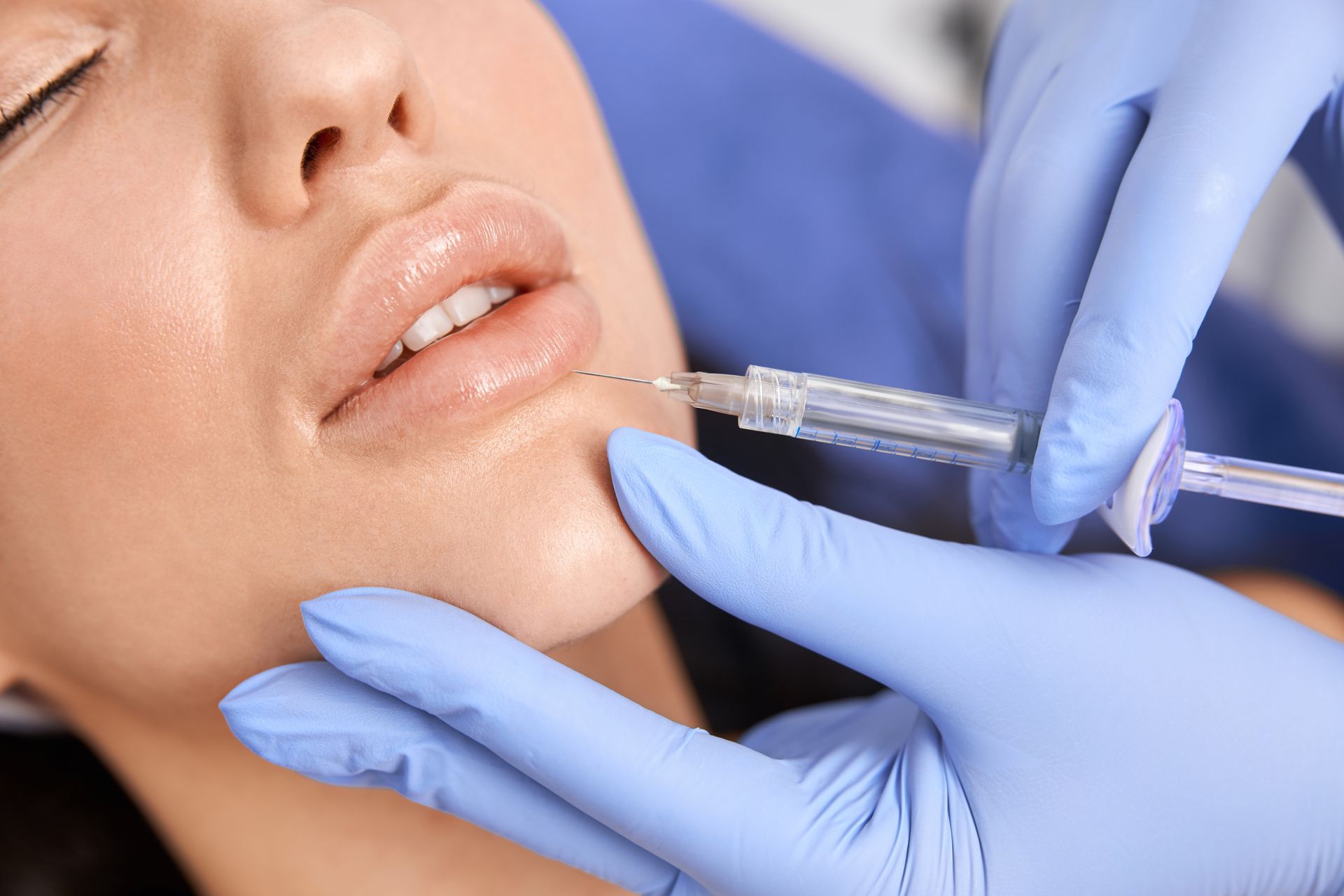 Person receiving lip injection; lips being injected with a syringe by gloved hands.