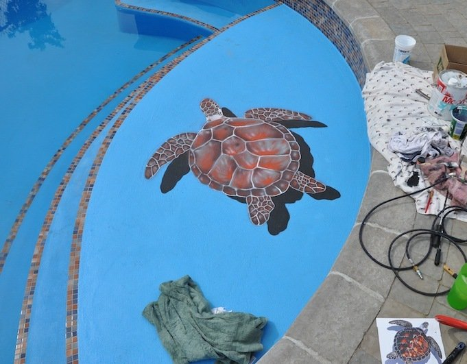 Une tortue de mer peinte sur le fond bleu d'une piscine, avec de l'eau et du matériel de peinture à proximité.