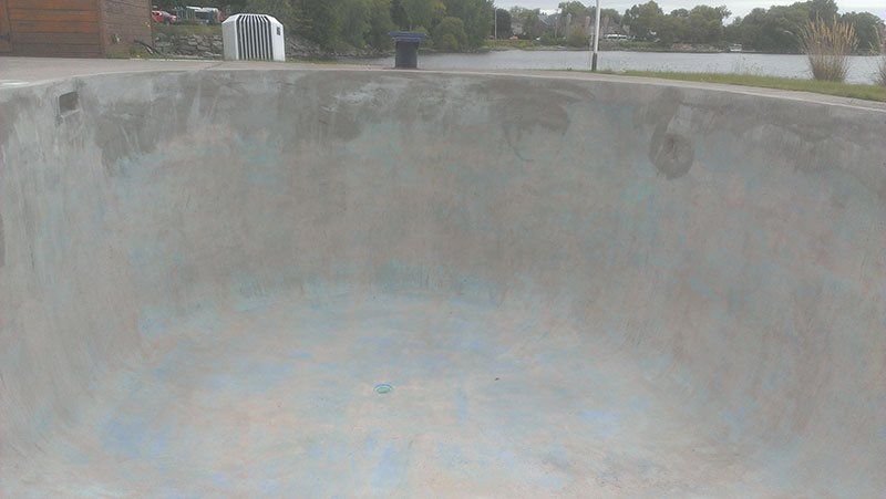 Un bol en béton dans un skate park avec une poubelle en arrière-plan.